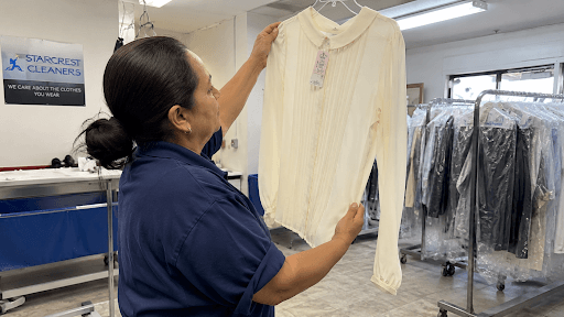 Dry cleaning technician inspecting a delicate silk garment under shop lighting as part of an eco-friendly dry cleaning assessment process.
